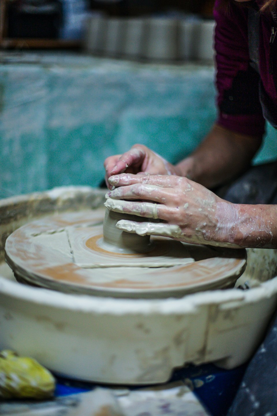 Hands covered in clay shape a pot on a pottery wheel.