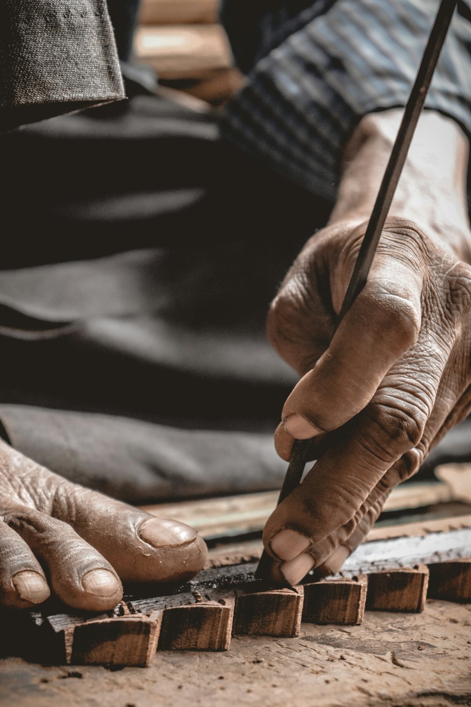 An artisan carves small wooden blocks with a metal tool.