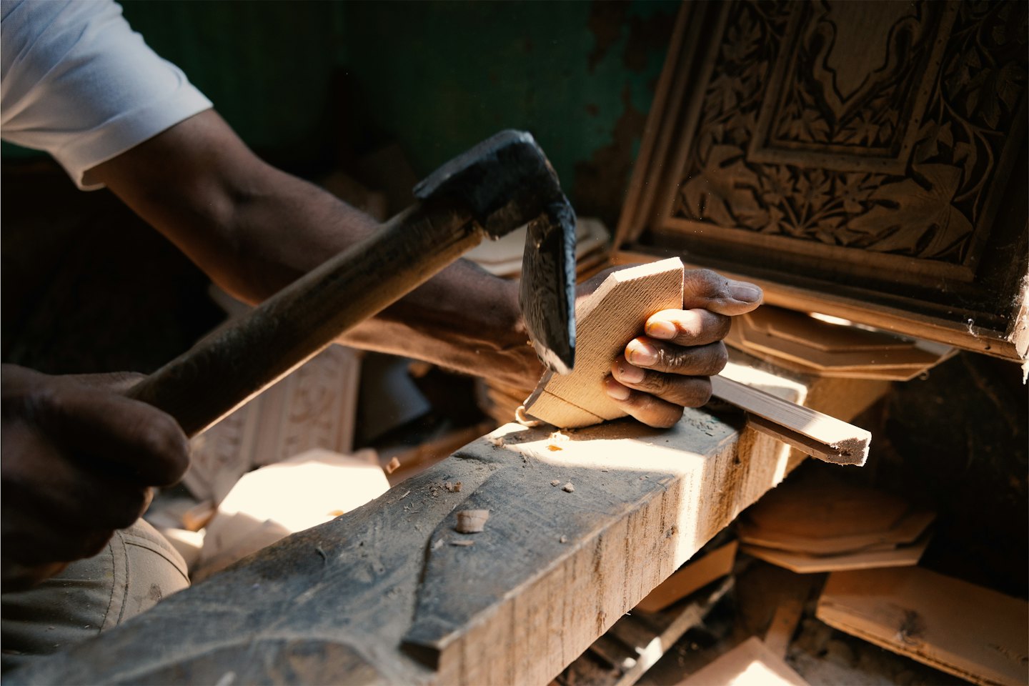 Craftsman carving intricate details into light wood with a tool.