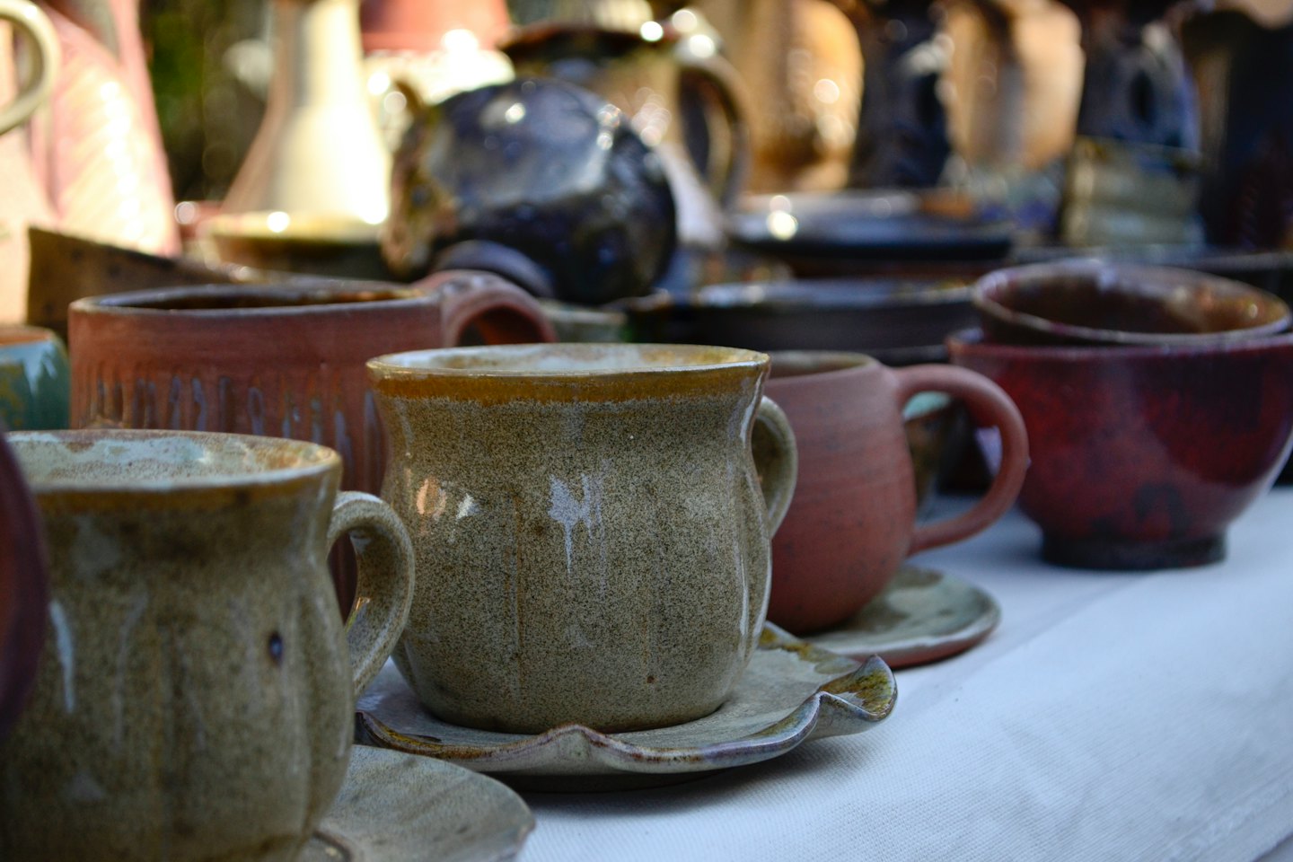 Handcrafted ceramic mugs and bowls arranged on a white tablecloth.