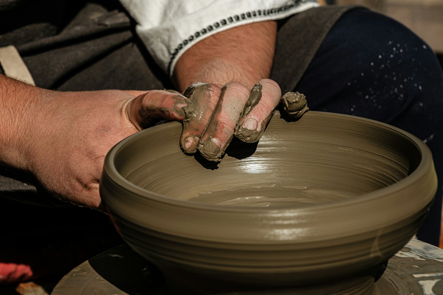 Hands covered in clay shape a bowl on a pottery wheel.